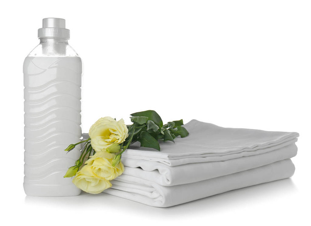 Pile de draps de lit propres et bouteille avec détergent sur fond blanc
 - Photo, image