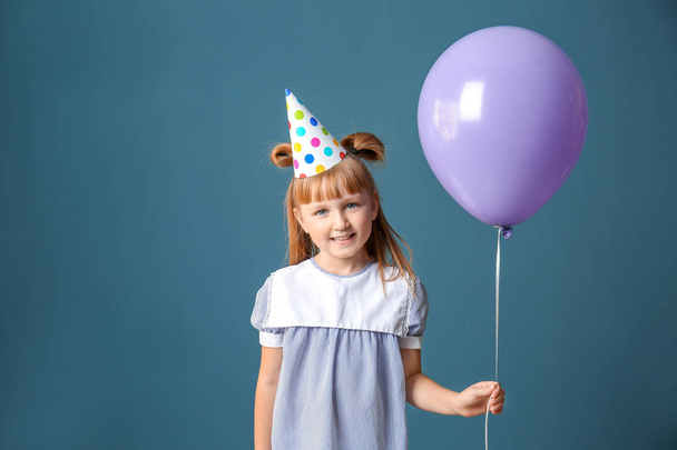 Cute little girl in Birthday hat and with balloon on color background - Photo, Image
