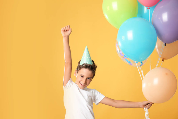 niedlichen kleinen Jungen in Geburtstagsmütze und mit Luftballons auf farbigem Hintergrund - Foto, Bild