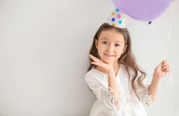 Cute little girl in Birthday hat and with balloon on light background - Valokuva, kuva
