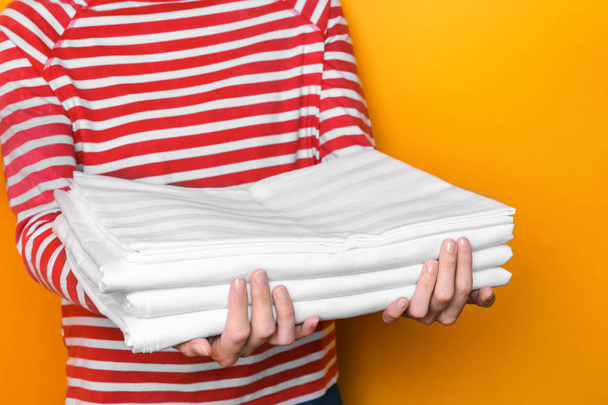 Woman holding stack of bed linen on color background - Fotó, kép