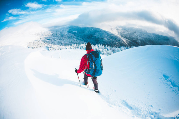 Un hombre en raquetas de nieve en las montañas en invierno. Un escalador con bastones de trekking camina por la nieve. Ascenso de invierno. Hermoso cielo con nubes
. - Foto, Imagen