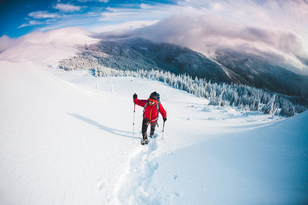 Człowiek w rakietach śnieżnych i kije trekking w górach. Wyjazd zimowy. Wspinaczka z wspinacz przeciwko piękne niebo z chmurami. Aktywny tryb życia. Wspinaczki górskiej przez śnieg. - Zdjęcie, obraz