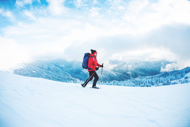 Um homem de sapatos de neve e paus de trekking nas montanhas. Viagem de inverno. Escalada de um alpinista contra um belo céu com nuvens. Estilo de vida ativo. Escalando a montanha através da neve
. - Foto, Imagem