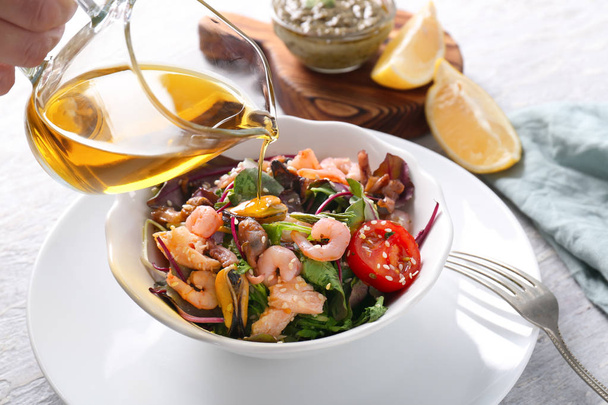 Woman pouring olive oil into bowl with delicious seafood salad on wooden table - Foto, imagen
