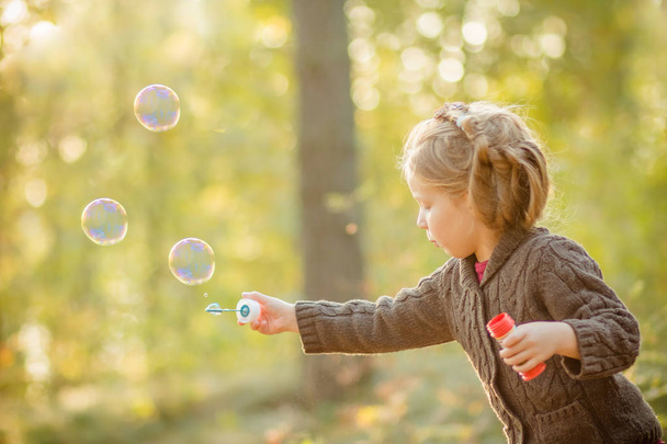Una niña soplando burbujas de jabón en el parque de otoño. tonificación de fondo para filtro instagram. El niño se divierte al aire libre, temporada de otoño, alegría y felicidad en el parque otoñal con la luz del sol. Concepto de libertad, hola
 - Foto, Imagen