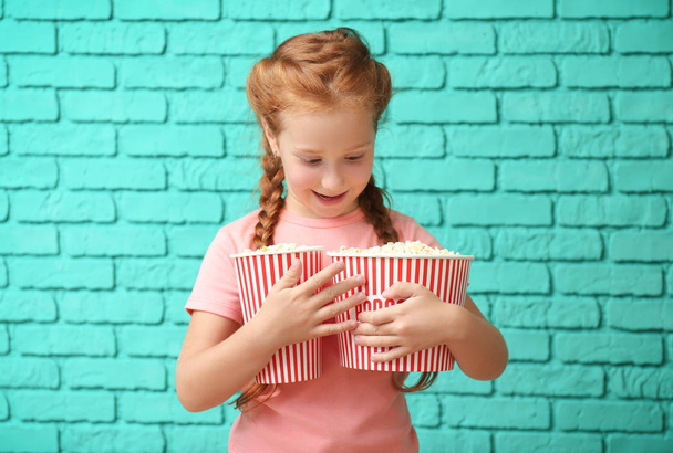 Nettes kleines Mädchen mit Tassen Popcorn gegen Ziegelwand - Foto, Bild
