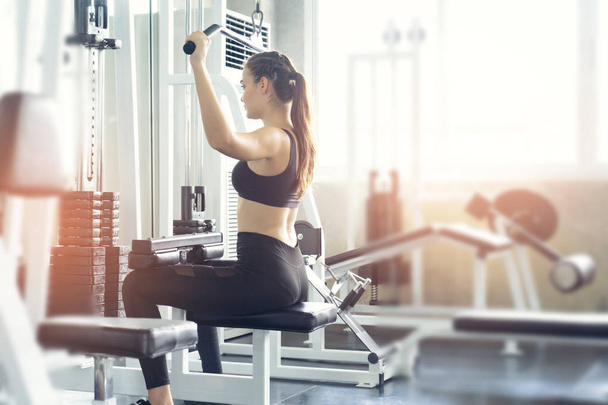 Muscular young woman with beautiful  body doing exercises with dumbbell. Sporty girl lifting weights in gym. - Foto, Imagem