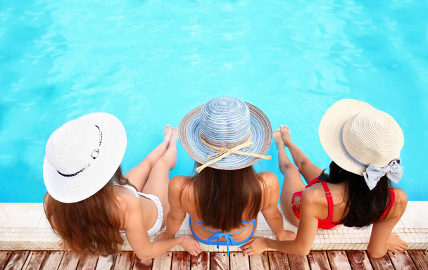 Mooie jonge vrouwen in kostuums in de buurt van zwembad zwemmen op zomerdag - Foto, afbeelding