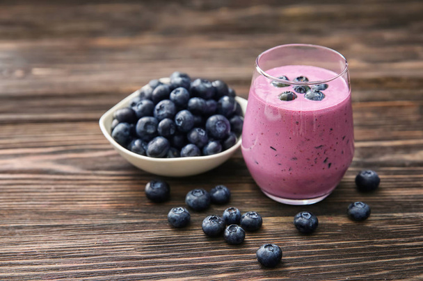 Glass of tasty blueberry smoothie and bowl with fresh berries on wooden table - Photo, Image