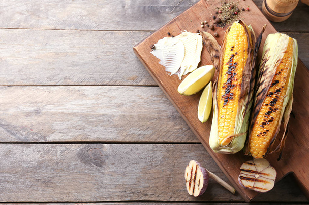 Tablero de madera con delicioso maíz a la parrilla en la mesa
 - Foto, Imagen