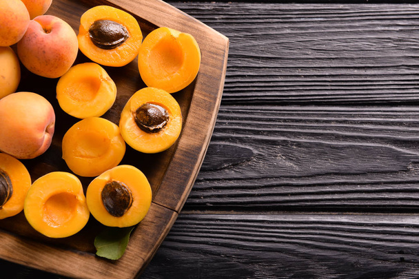Деревянная тарелка со сладкими спелыми абрикосами на столе, вид сверху
 - Фото, изображение