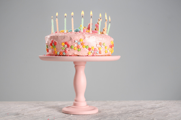 Stand with tasty birthday cake and burning candles on table - Foto, Bild