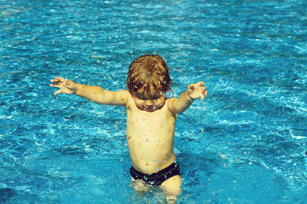 Cute baby boy with wet hair sprinkles water in pool - Foto, immagini
