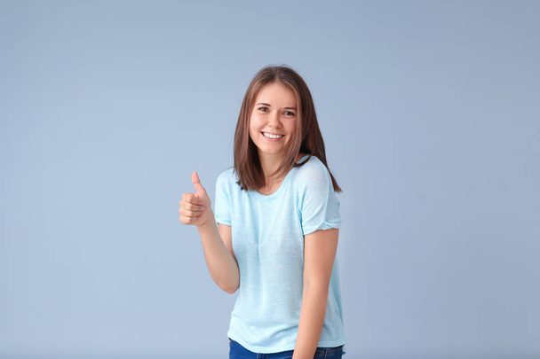 schöne junge Frau zeigt Daumen-hoch-Geste auf hellem Hintergrund - Foto, Bild