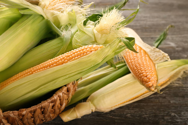 Wicker basket with fresh corn cobs on wooden table, closeup - Photo, Image
