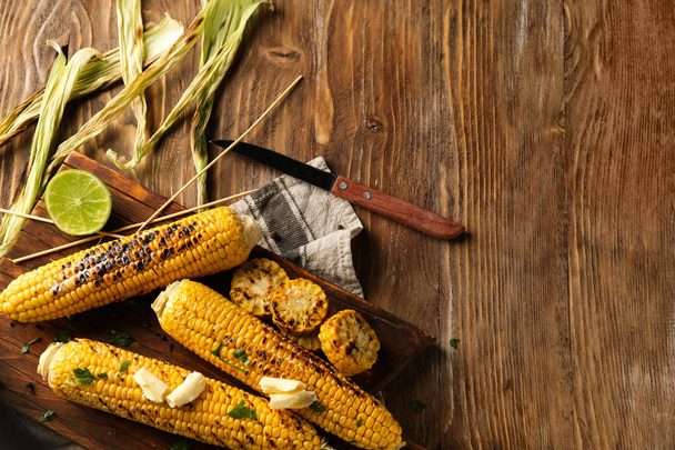 Sabrosas mazorcas de maíz a la parrilla en mesa de madera
 - Foto, Imagen