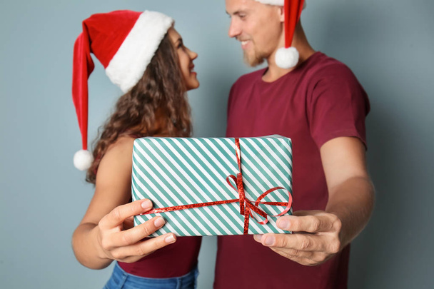 Cute young couple with Christmas present on color background - Photo, Image