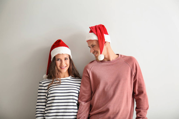 Portrét roztomilý mladý pár v Santa klobouky na světlé pozadí - Fotografie, Obrázek