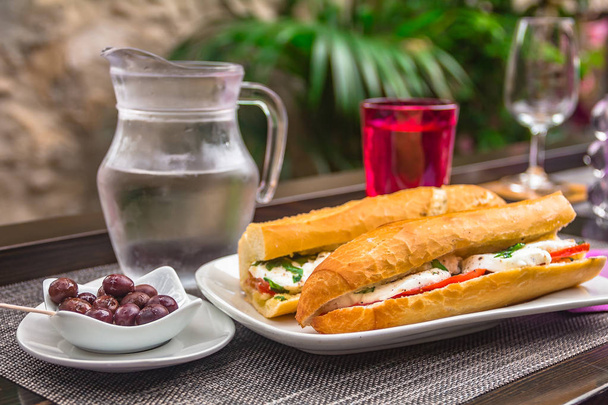 Caprese friss vagy paradicsomos és mozzarella baguette szendvics és olajbogyó, a dél-franciaországi falu Eze-kültéri utcai kávézóban egy asztalnál - Fotó, kép
