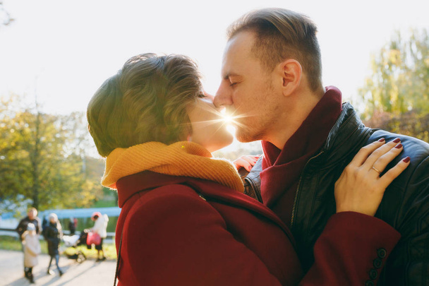 天気の良い屋外で秋の市の公園で散歩に背後にある太陽とのキスを受け入れる温かい普段着の愛女性男性で若いカップルのクローズ アップ。愛の関係家族のライフ スタイル コンセプト - 写真・画像