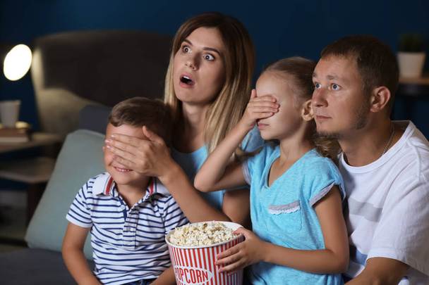 Family eating popcorn while watching scary movie in evening - Фото, изображение