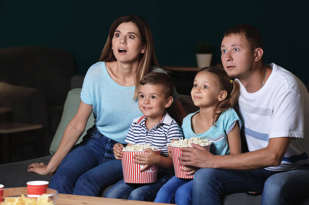Perhe syö popcornia katsoessaan televisiota illalla
 - Valokuva, kuva