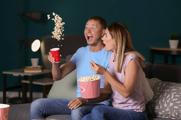 Happy emotional couple eating popcorn while watching TV in evening - Photo, Image