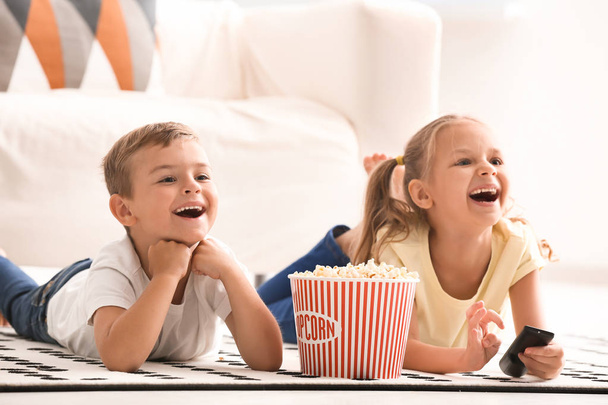 Cute children eating popcorn while watching TV at home - 写真・画像