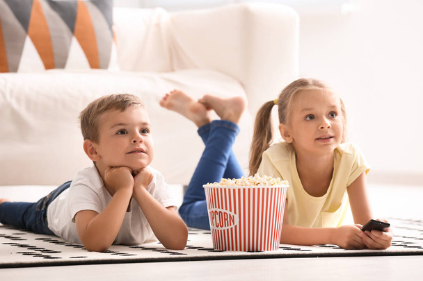 Χαριτωμένα παιδιά τρώνε ποπ κορν βλέποντας τηλεόραση στο σπίτι - Φωτογραφία, εικόνα