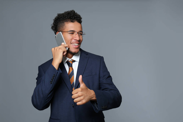 Handsome African-American businessman talking by mobile phone on grey background - Foto, Imagem