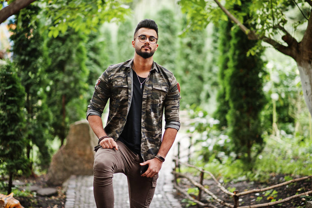 Awesome beautiful tall ararbian beard macho man in glasses and military jacket posed outdoor. - Фото, изображение