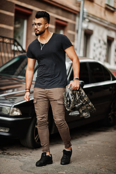 Awesome beautiful tall ararbian beard macho man in glasses and black t-shirt walking against business car. - Foto, afbeelding