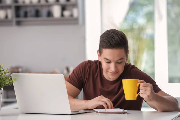 Молодой фрилансер пьет кофе во время работы на кухне
 - Фото, изображение