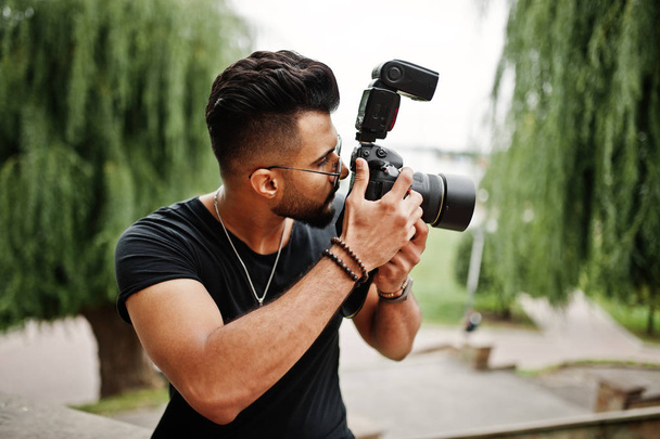 Awesome beautiful tall ararbian beard macho man photographer in glasses and black t-shirt with professional camera at hands. - Foto, Bild