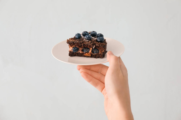 Frau hält Teller mit Stück Blaubeer-Schokoladenkuchen auf hellem Hintergrund - Foto, Bild