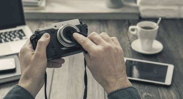 Hipster photographer at home sitting at desk and cleaning his camera lens with a cloth, point of view shot - 写真・画像