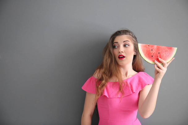 Beautiful young woman with slice of tasty watermelon on grey background - Photo, Image