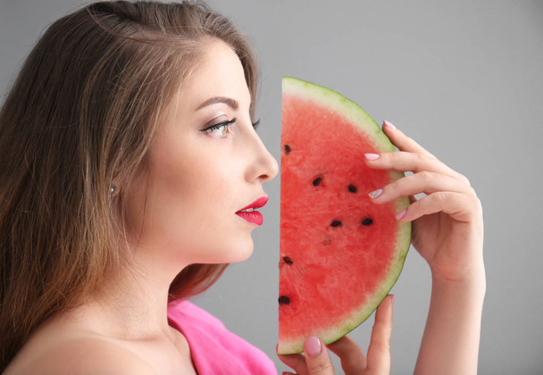 Gyönyörű fiatal nő, szelet, ízletes görögdinnye szürke háttér - Fotó, kép