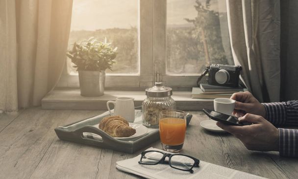 Хипстерский человек завтракает дома рано утром, он использует смартфон, здоровый образ жизни и технологическую концепцию
 - Фото, изображение