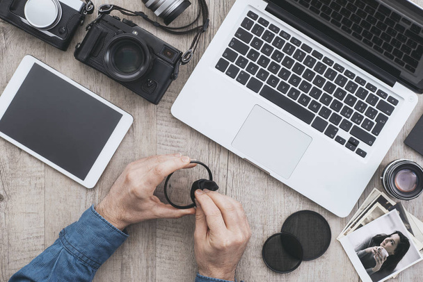 Professional photographic equipment and laptop on a desktop, a photographer is carefully cleaning a filter, flat lay - Fotoğraf, Görsel
