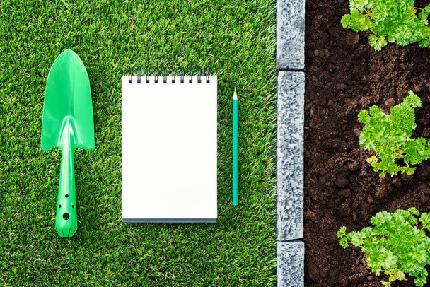 Gardener's to-do list: blank notepad, shovel and plants growing on the soil - Photo, Image