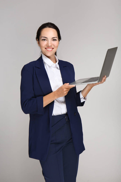 Beautiful businesswoman with laptop on grey background - Foto, afbeelding