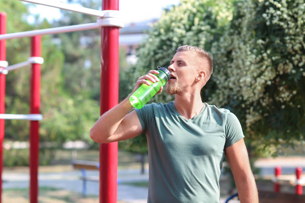 Sporty young man drinking water after training outdoors - Fotó, kép