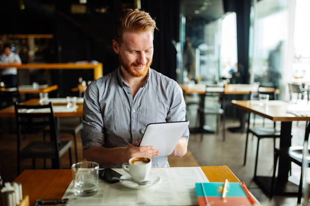 Handsome smart businessman holding tablet in cafe - Фото, изображение