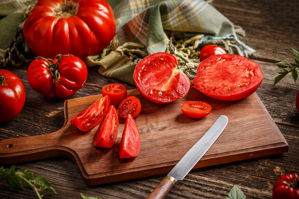 Whole red tomatoes and slice of tomatoes on wooden cutting board - Фото, изображение
