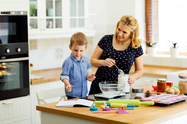 Child helping mother prepare muffins in kitchen - Photo, image