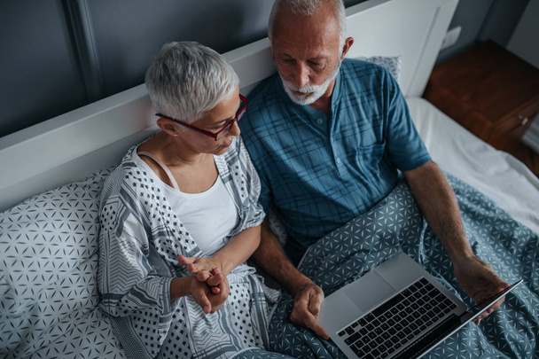 Senior couple surfing the net in bed. - Foto, afbeelding
