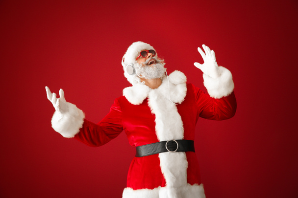 Portrait of cool Santa Claus listening to music on color background - Foto, afbeelding