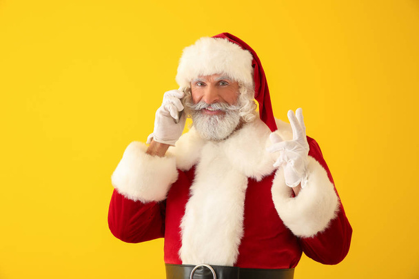 Santa Claus talking by mobile phone on color background - Photo, Image